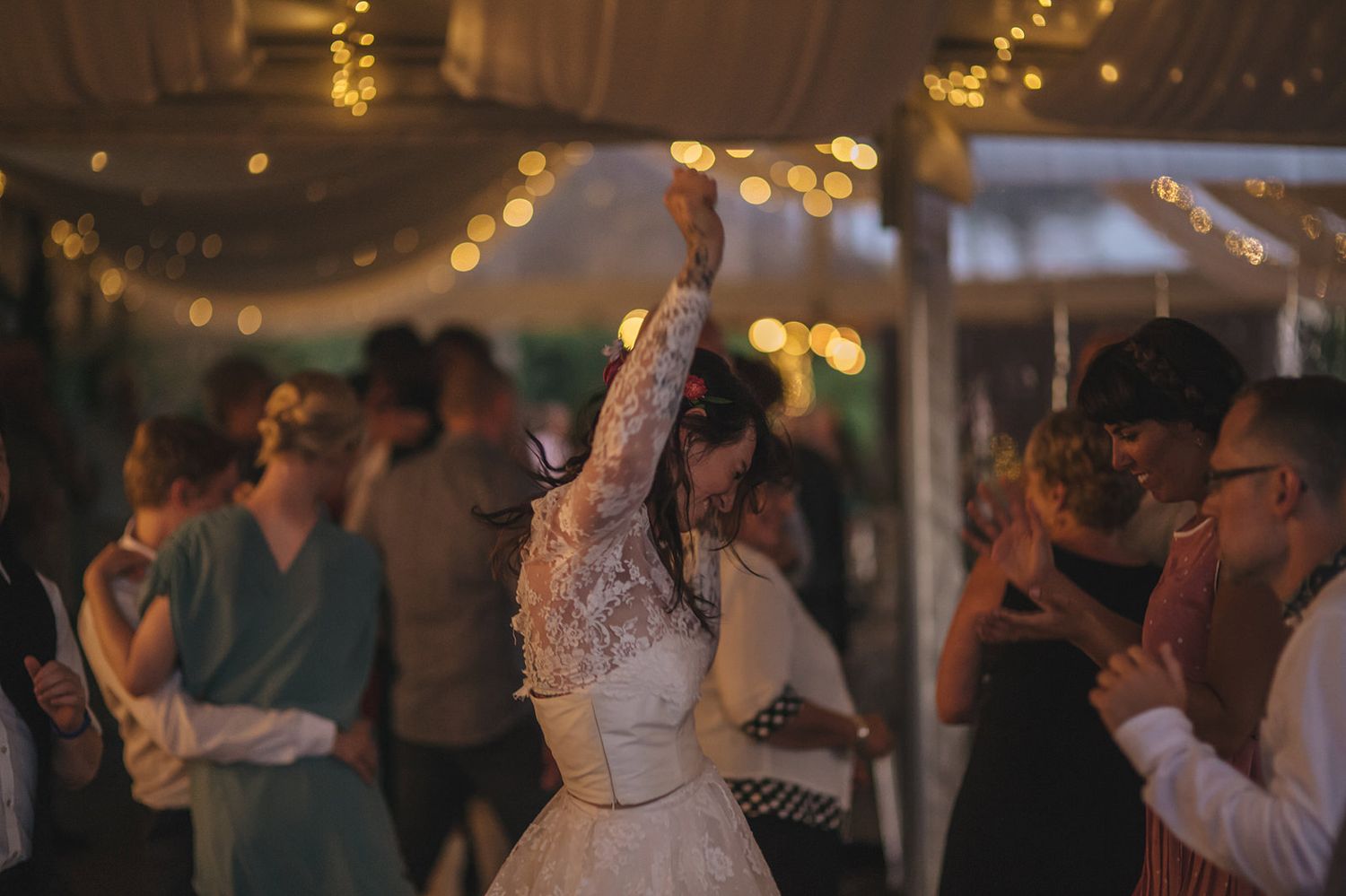 Couples dancing together during a romantic dimly lit celebration with string lights and an intimate atmosphere.