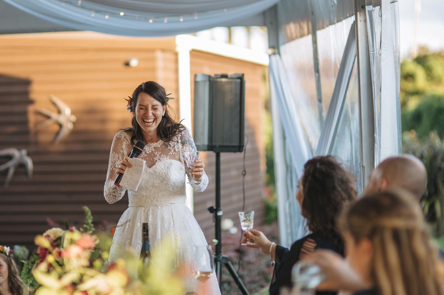 A bride laughs joyfully during golden hour at an outdoor wedding reception venue decorated with elegant draping.