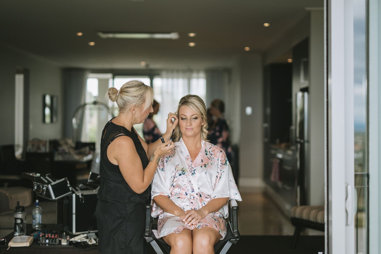 Professional makeup artist works with client in salon chair during getting ready preparation session.