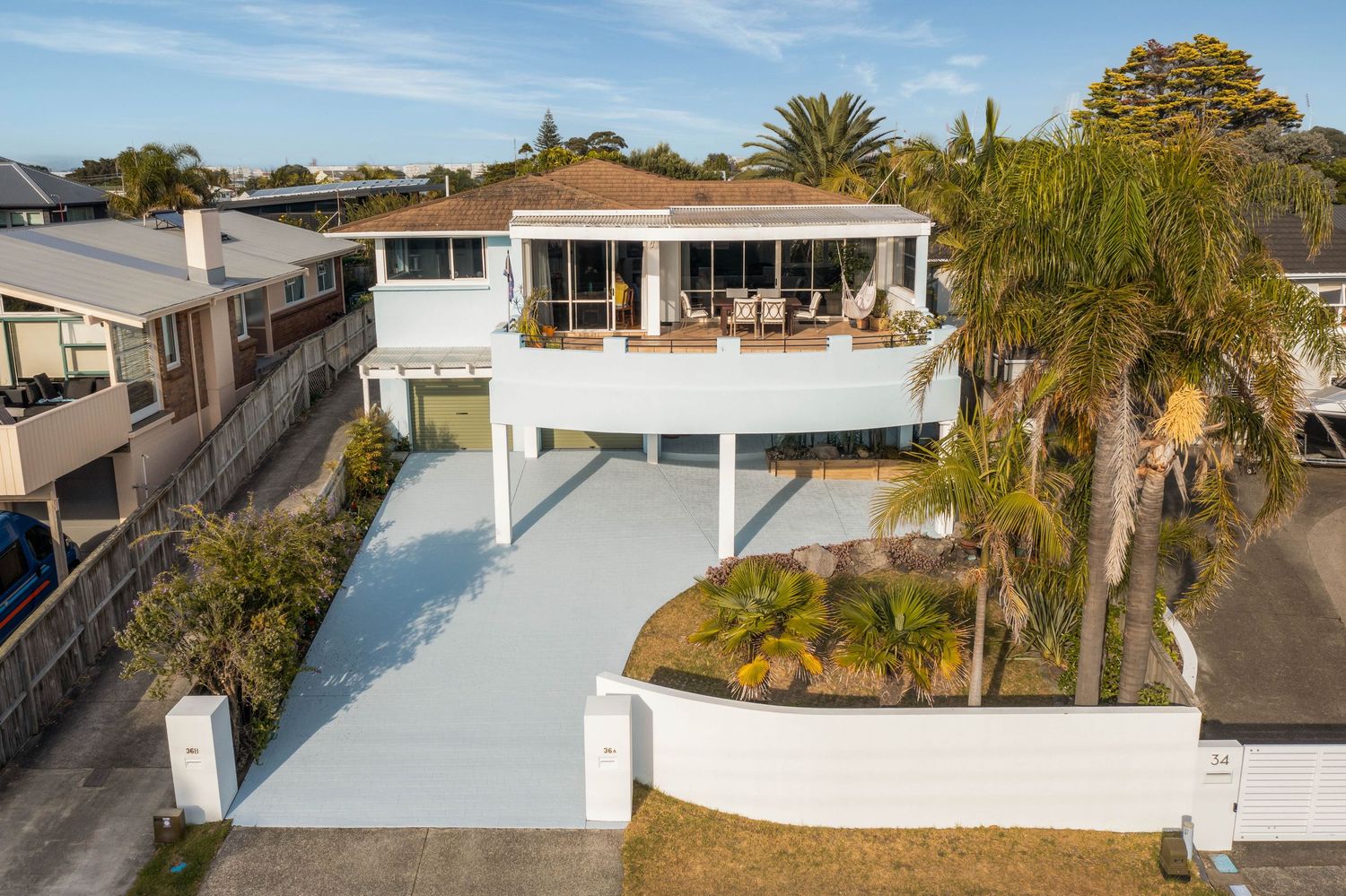 Aerial view of a modern white house with palm trees and landscaping in a residential neighborhood.