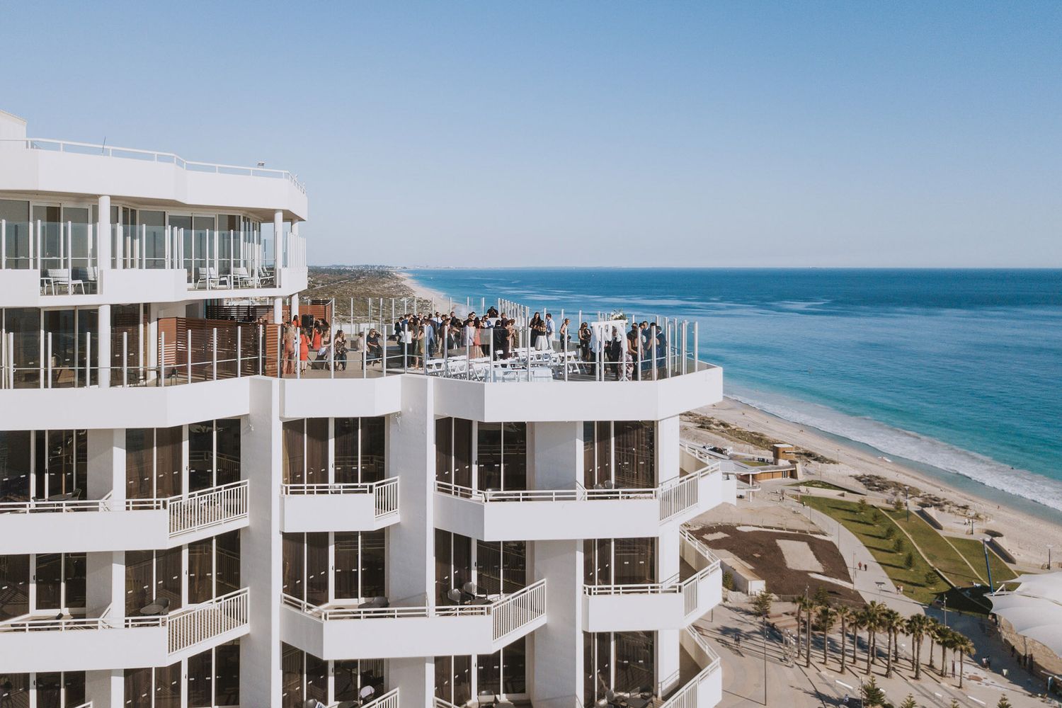Modern white beachfront condominium building overlooking turquoise ocean waters and sandy coastline on a sunny day.