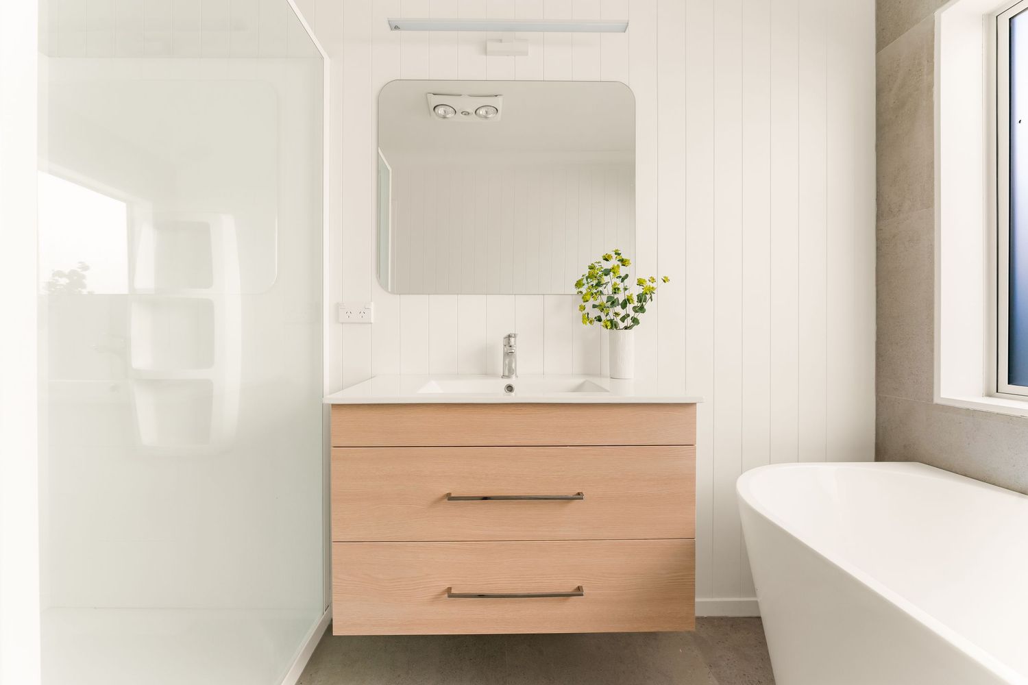 Modern bathroom featuring floating wood vanity, large mirror, and freestanding white bathtub.