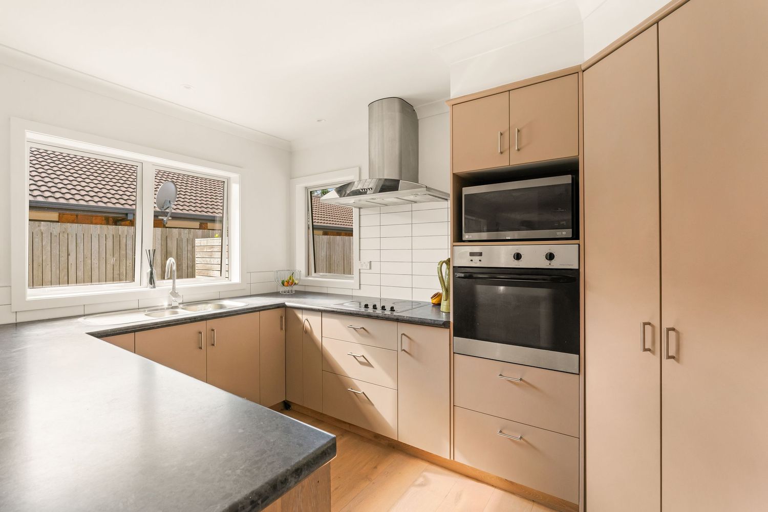Modern beige kitchen features white cabinets, dark countertops and stainless steel appliances in clean contemporary design.