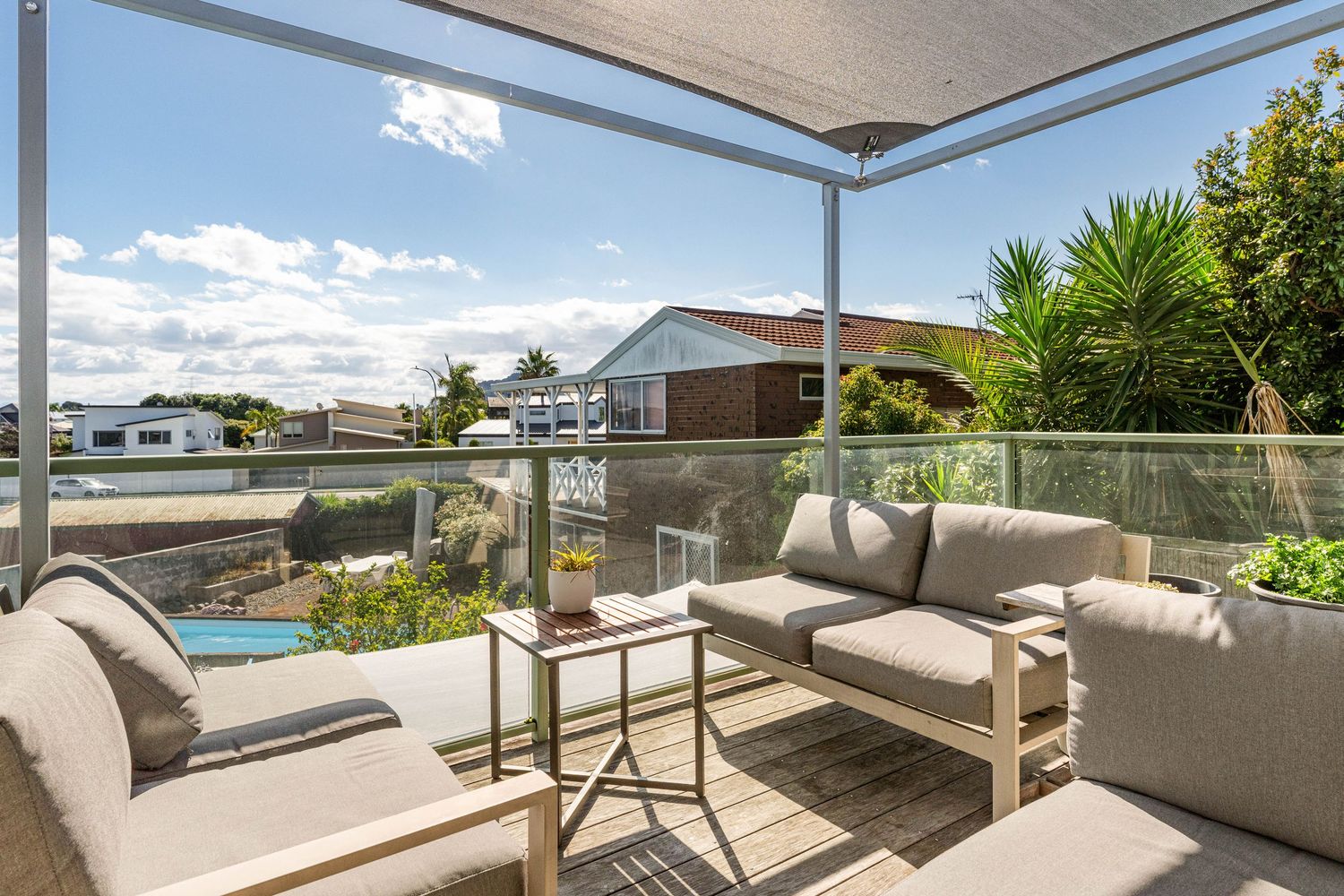Covered outdoor patio with comfortable grey seating furniture overlooking residential neighborhood and blue skies.