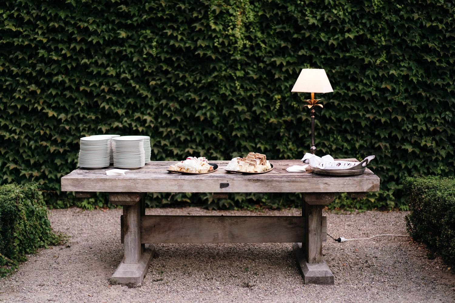 Row of empty wooden benches along gravel path with green hedge background.
