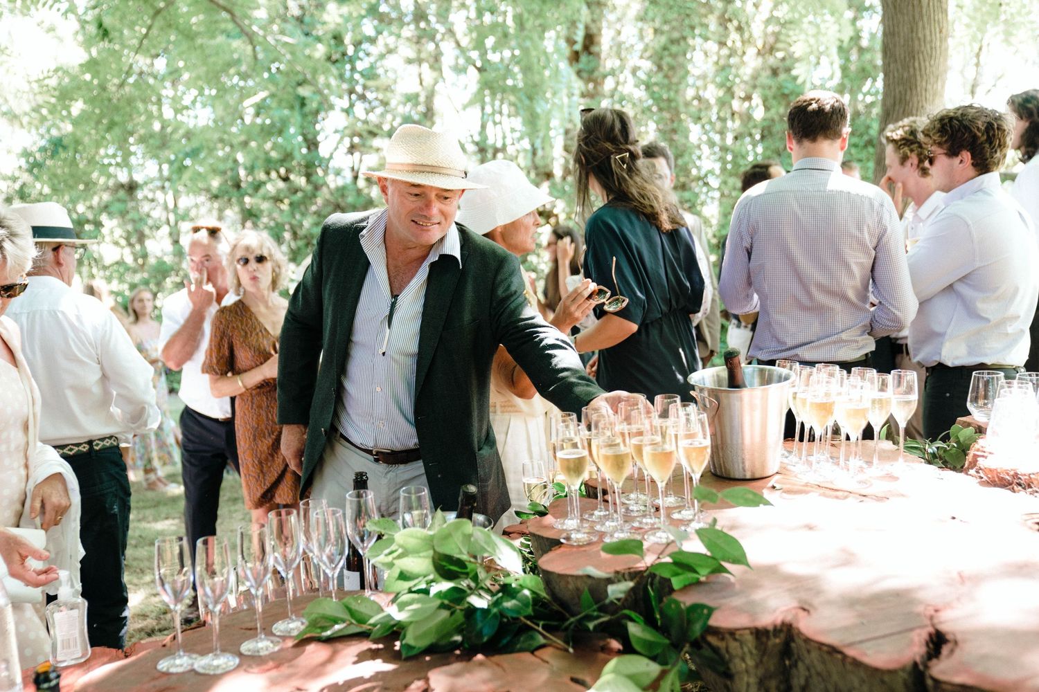 Wedding reception guests mingling around an elegantly set outdoor table with glassware.