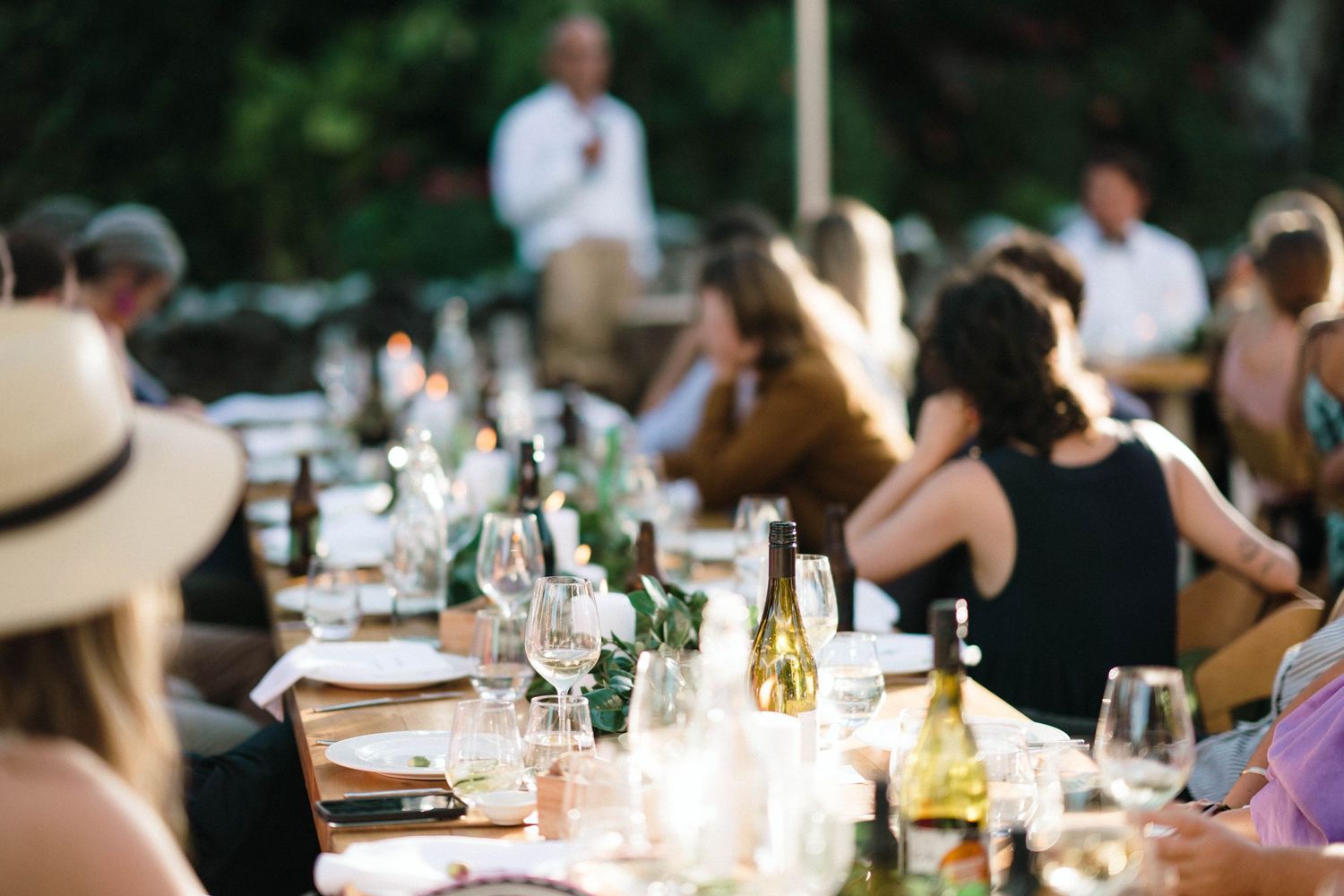 Elegantly set dinner tables at an outdoor wedding reception with wine bottles and floral centerpieces.