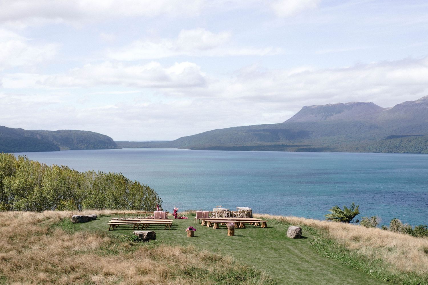 Scenic coastal landscape with mountains and water, featuring a small gathering area on the hillside.