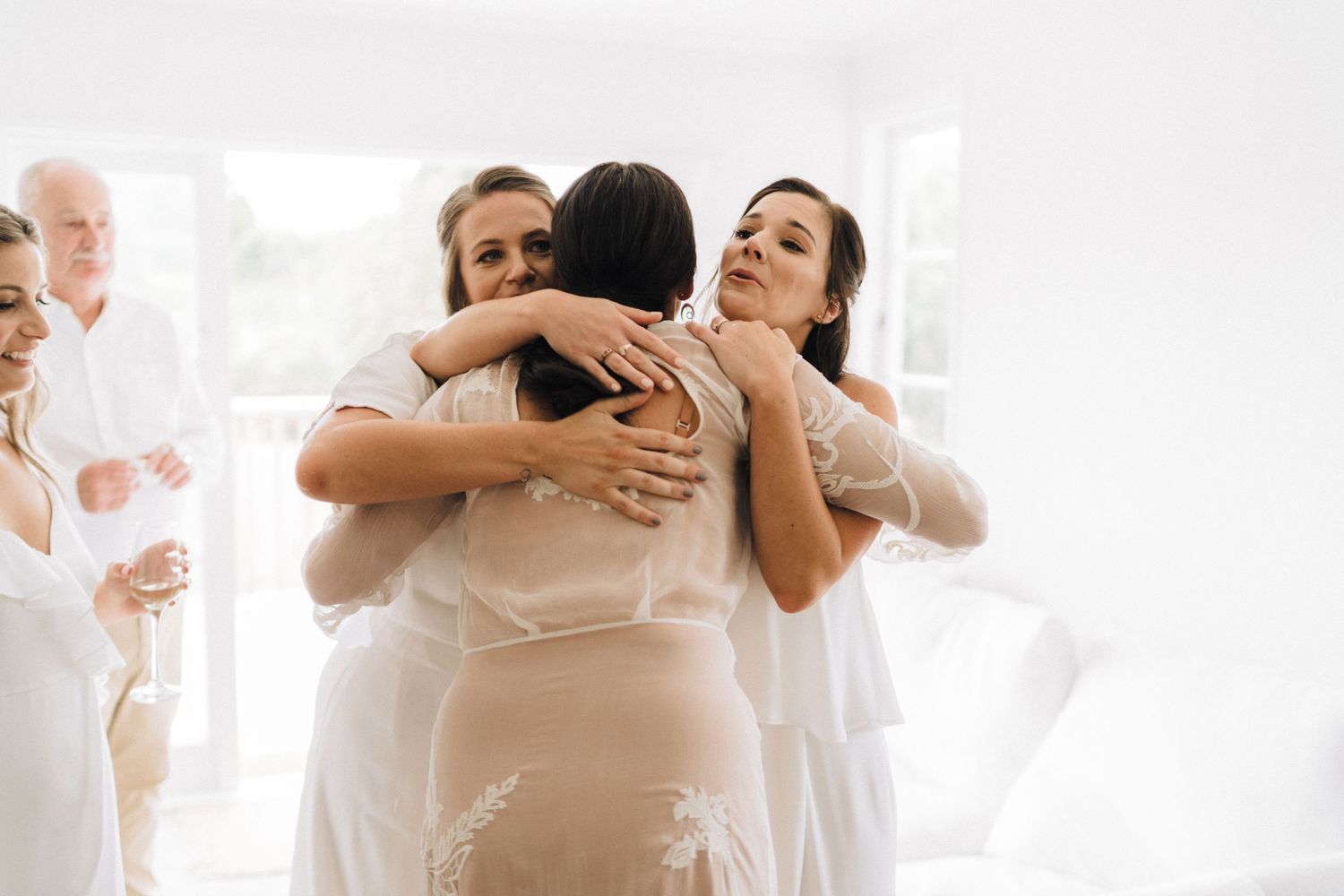 Wedding guests share emotional embrace during a dance in an light-filled venue.
