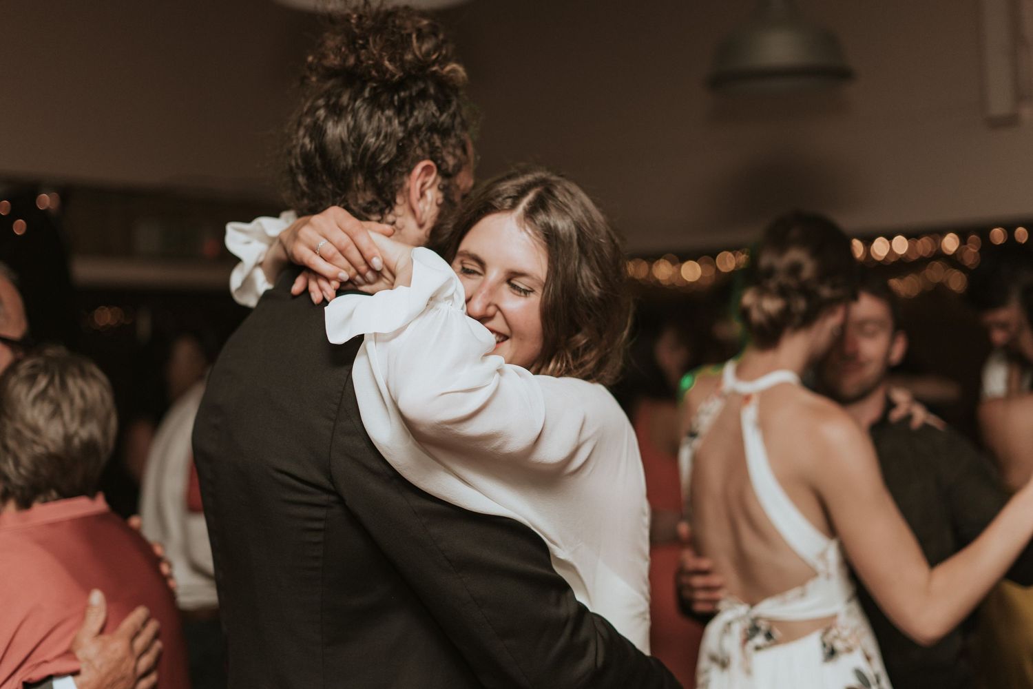 Romantic first dance between newlyweds surrounded by guests at an intimate indoor wedding reception with warm lighting.