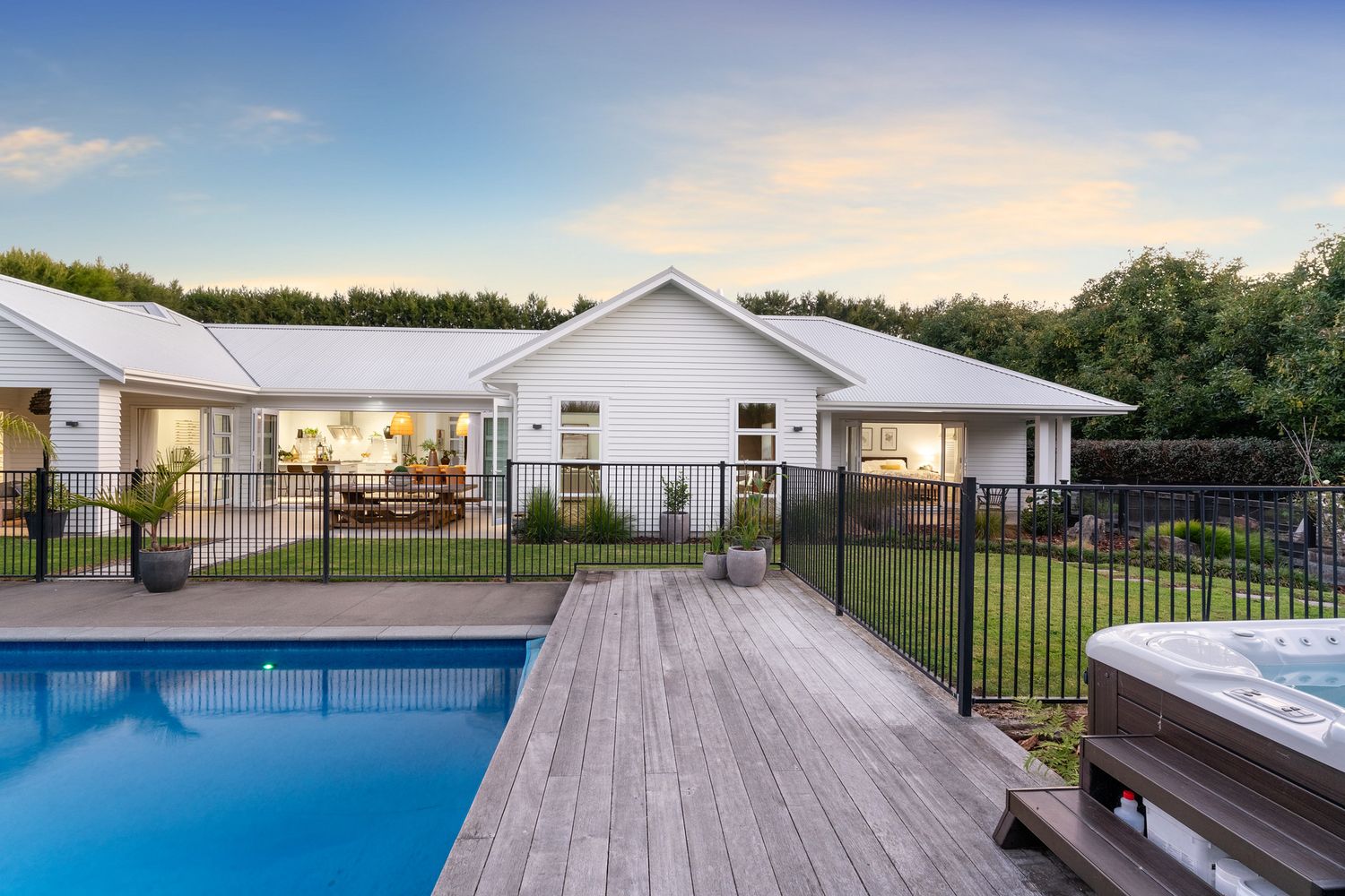 Contemporary white house with illuminated pool deck and fenced swimming area at sunset.