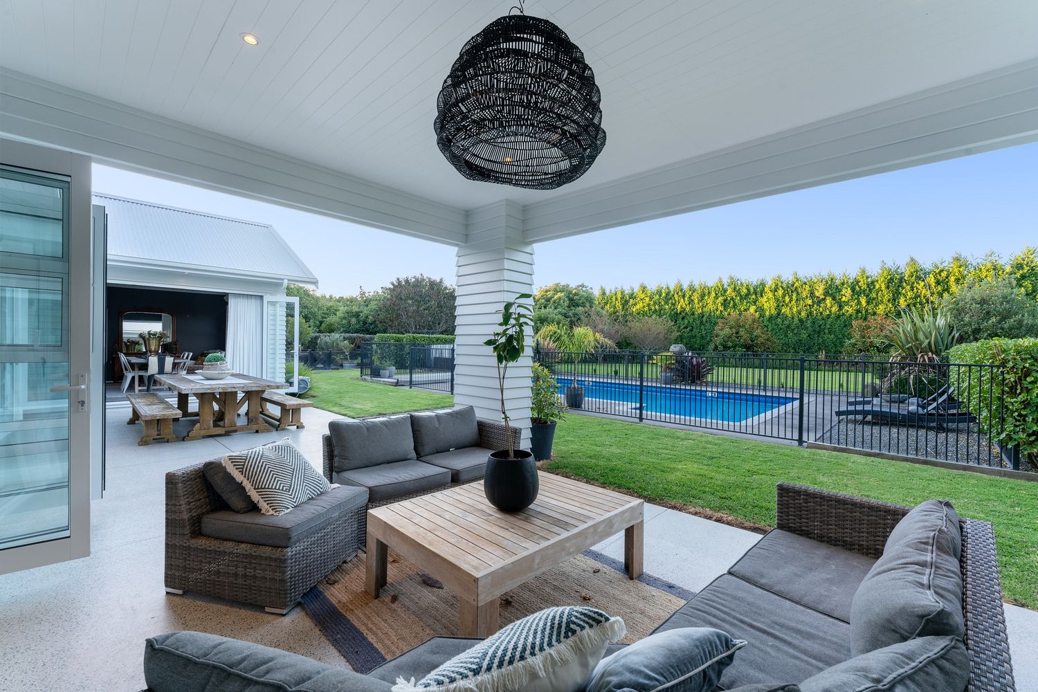 Contemporary covered patio with gray outdoor furniture overlooking swimming pool and garden.