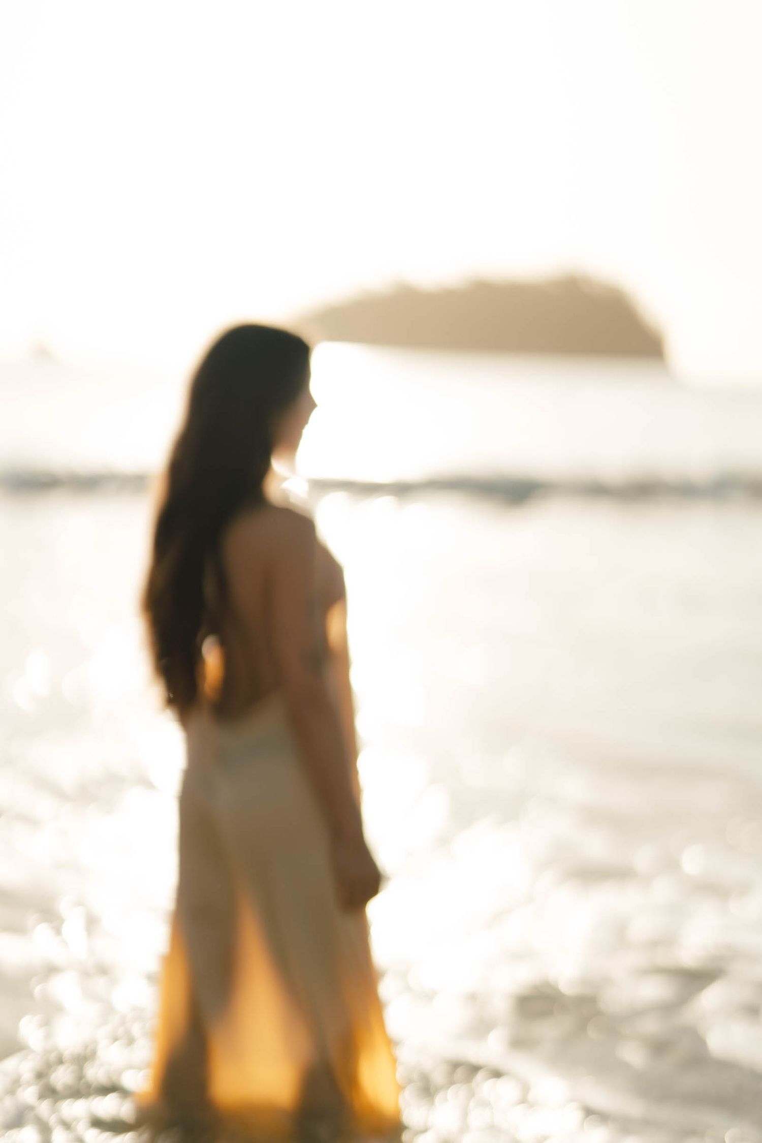 Silhouetted figure stands in ocean waves during a misty sunset.