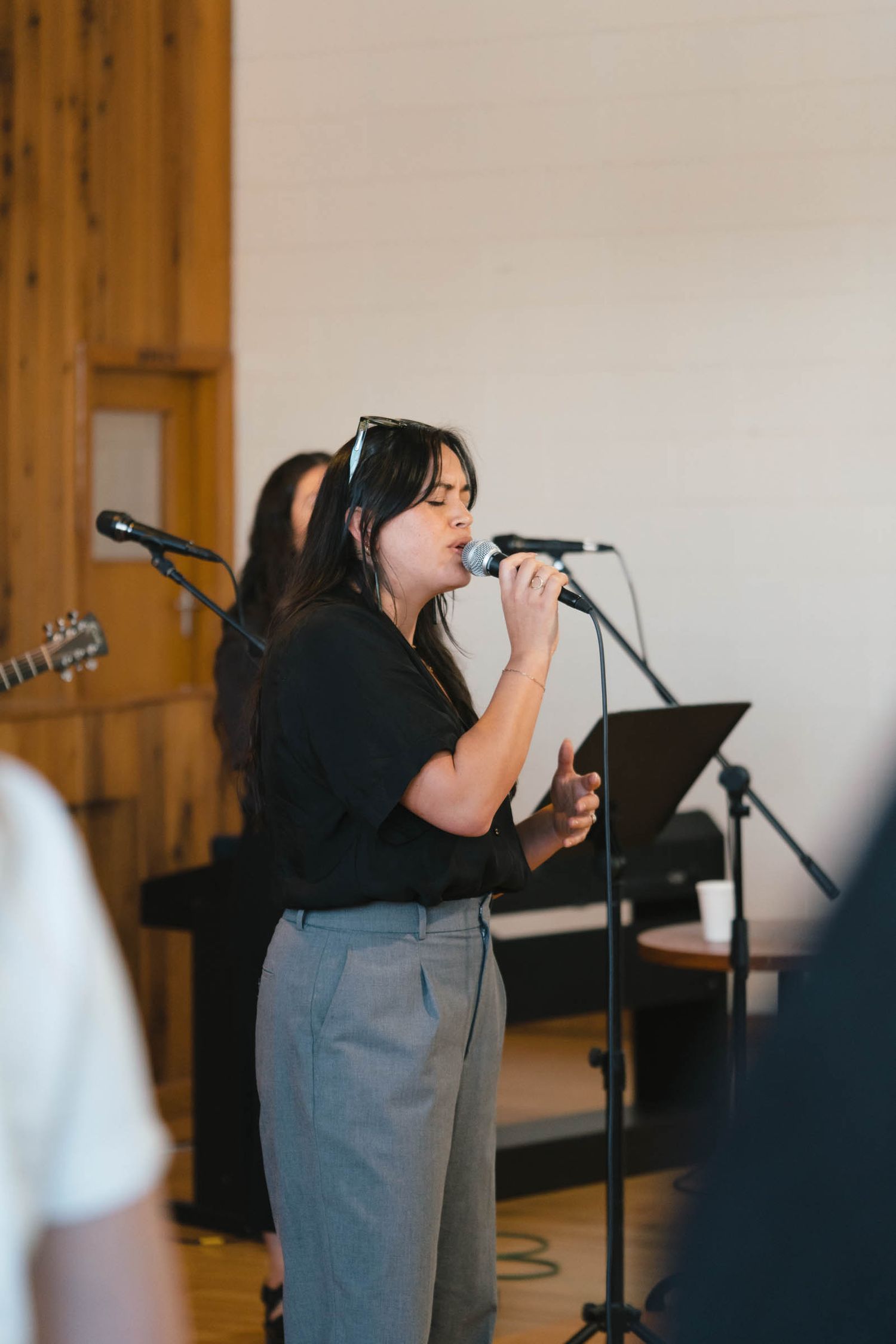 A singer performing with a microphone stand in front of a wooden wall.