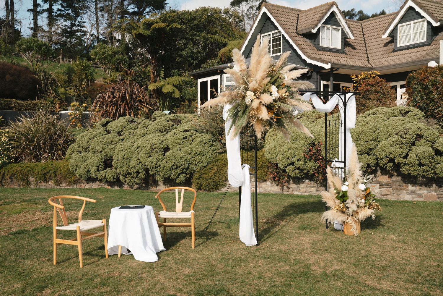 Row of romantic wooden chairs and hanging drapes set up for an outdoor garden wedding ceremony overlooking coastal scenery.