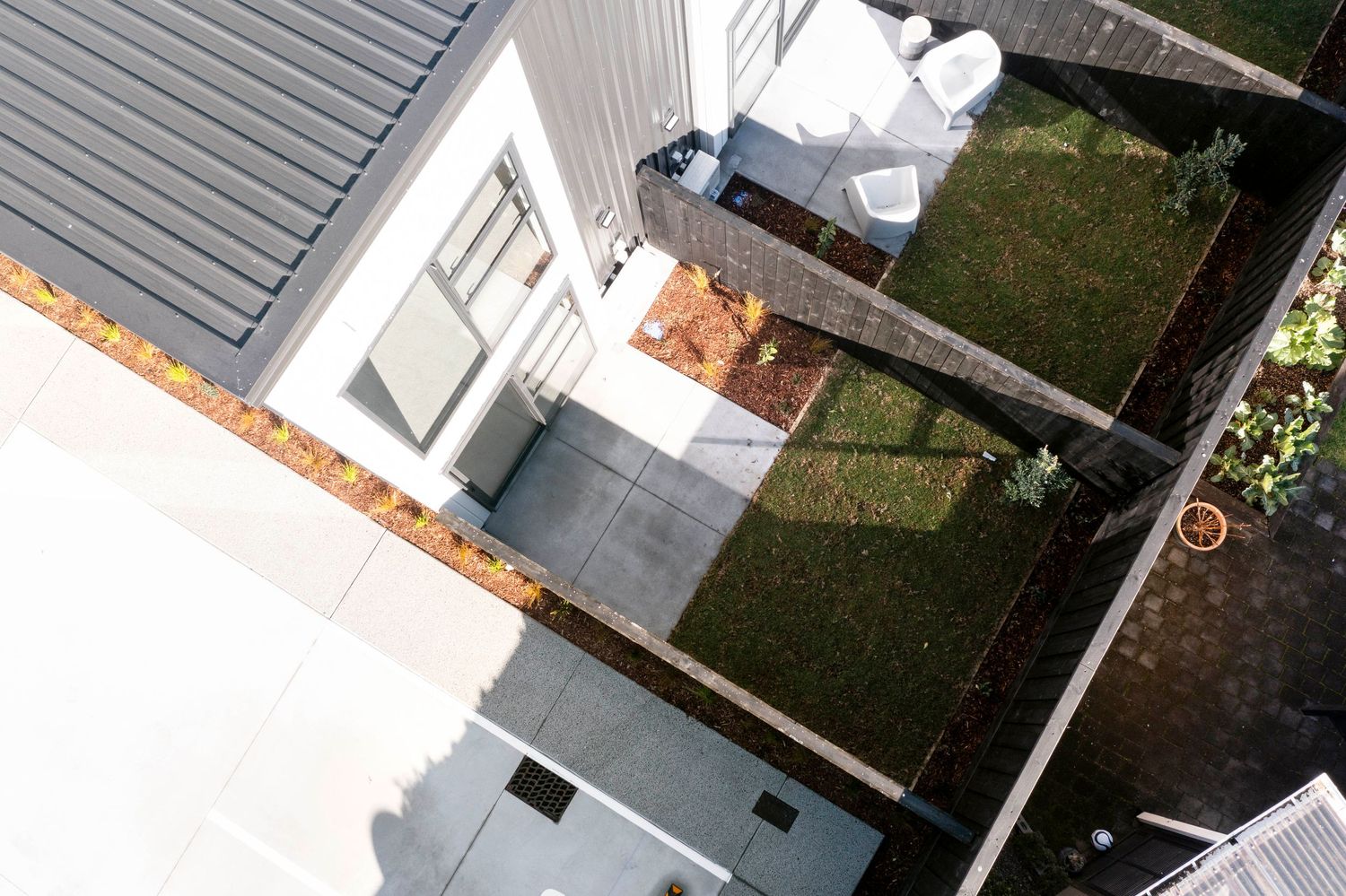 Aerial view of a house's exterior showing grey siding, landscaping, and a patio area.