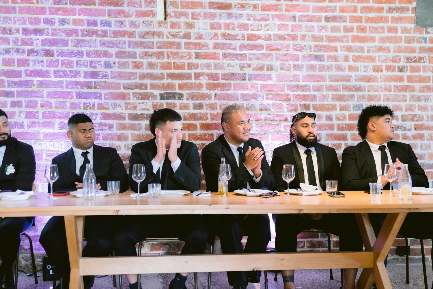 Wedding party seated at a long table against exposed brick wall with purple uplighting.