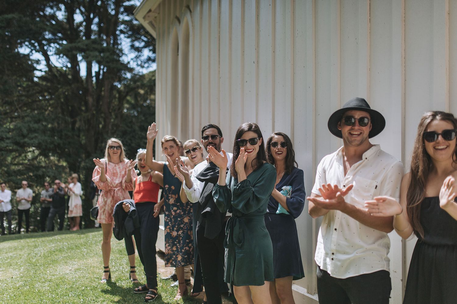 A group of wedding party members dressed in casual attire pose together outside a white columned building.