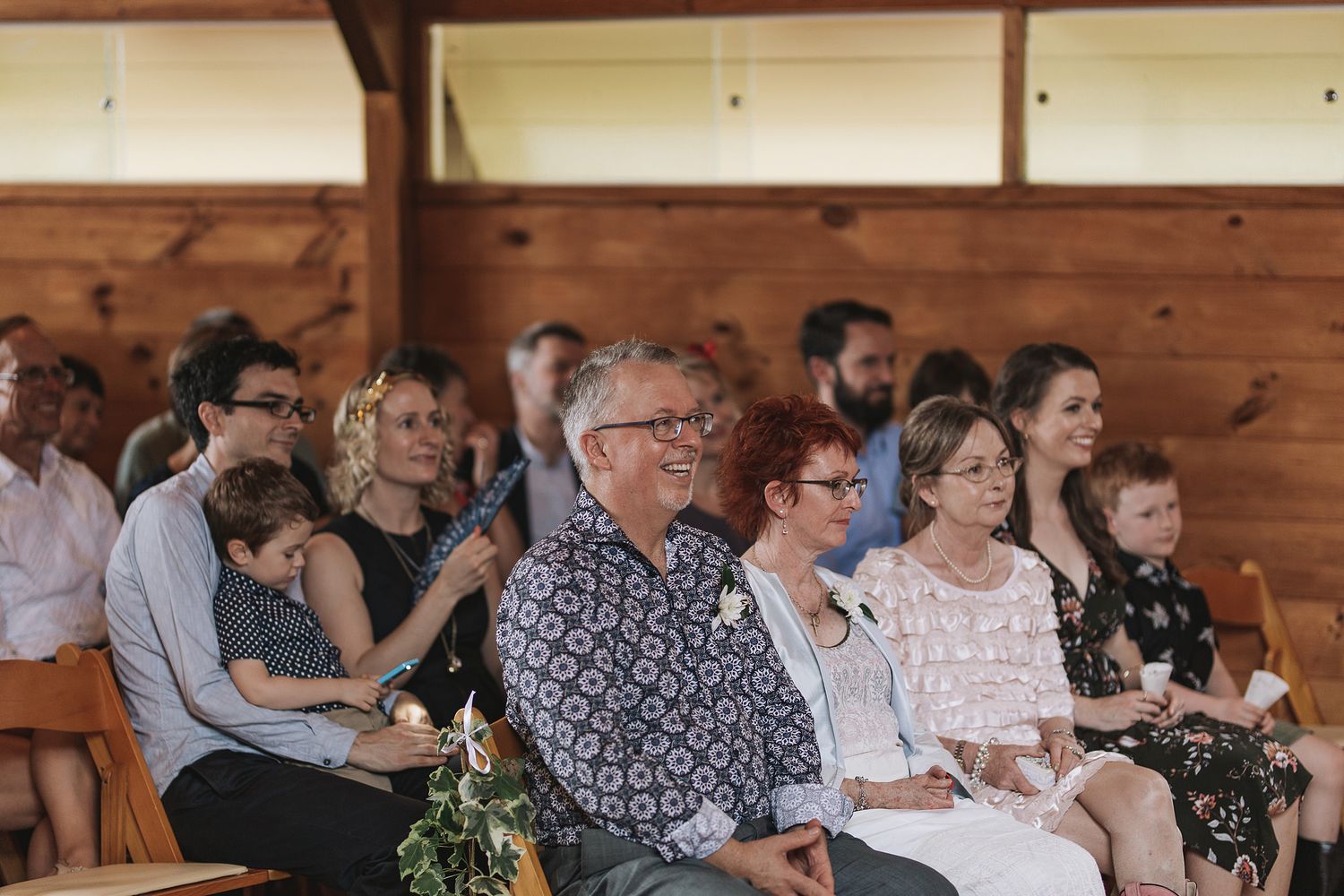 A crowd of guests watches attentively during a celebration event in a rustic wooden venue.