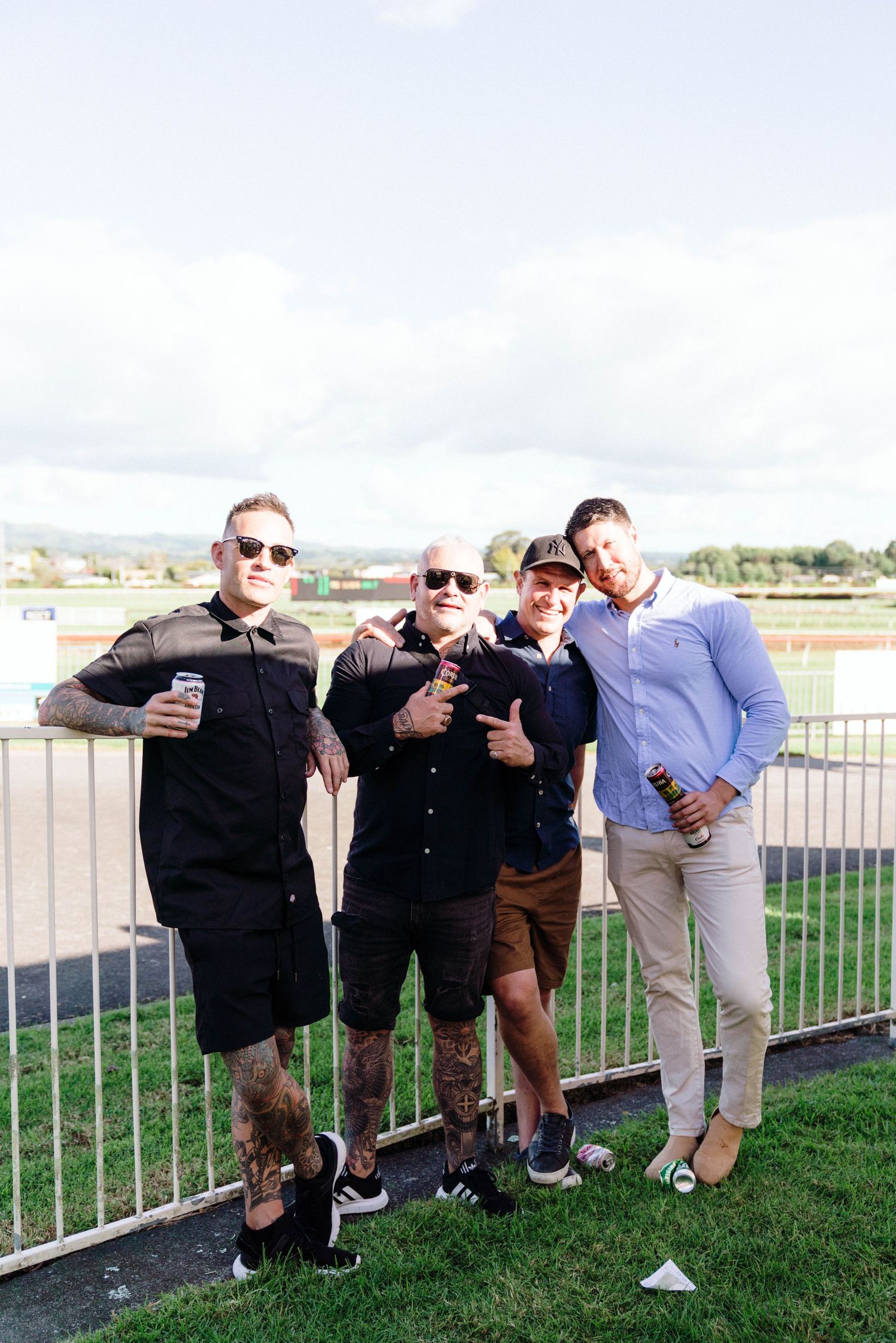 Group of friends in casual wear pose with drinks at an outdoor venue.