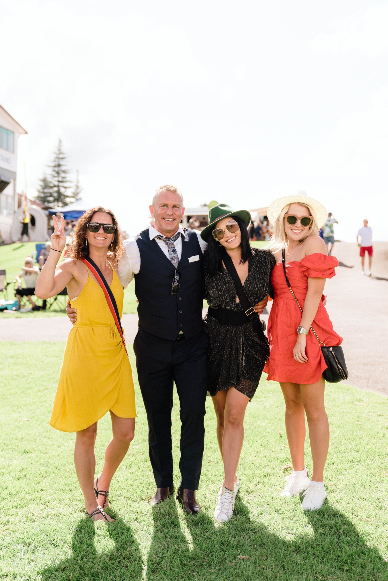 Friends in colorful summer outfits pose together on grass at an outdoor event.