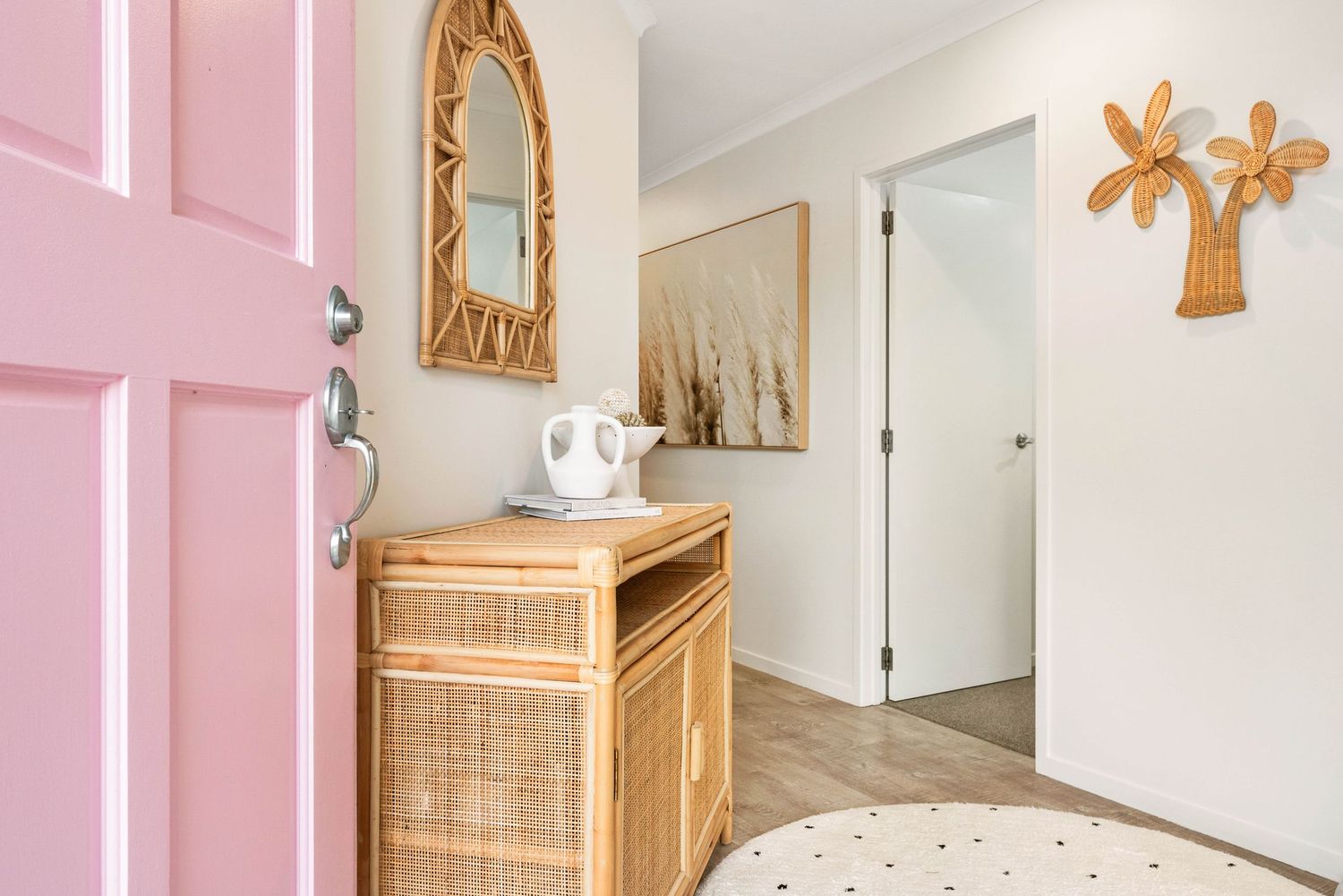 Modern hallway interior with pink door, bamboo console table, decorative mirror and wooden wall art.