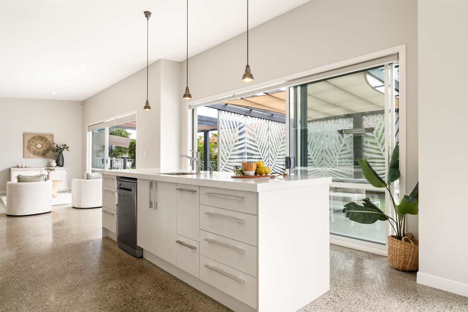 Modern white kitchen interior with polished concrete floors, pendant lighting and large sliding glass doors opening to patio.