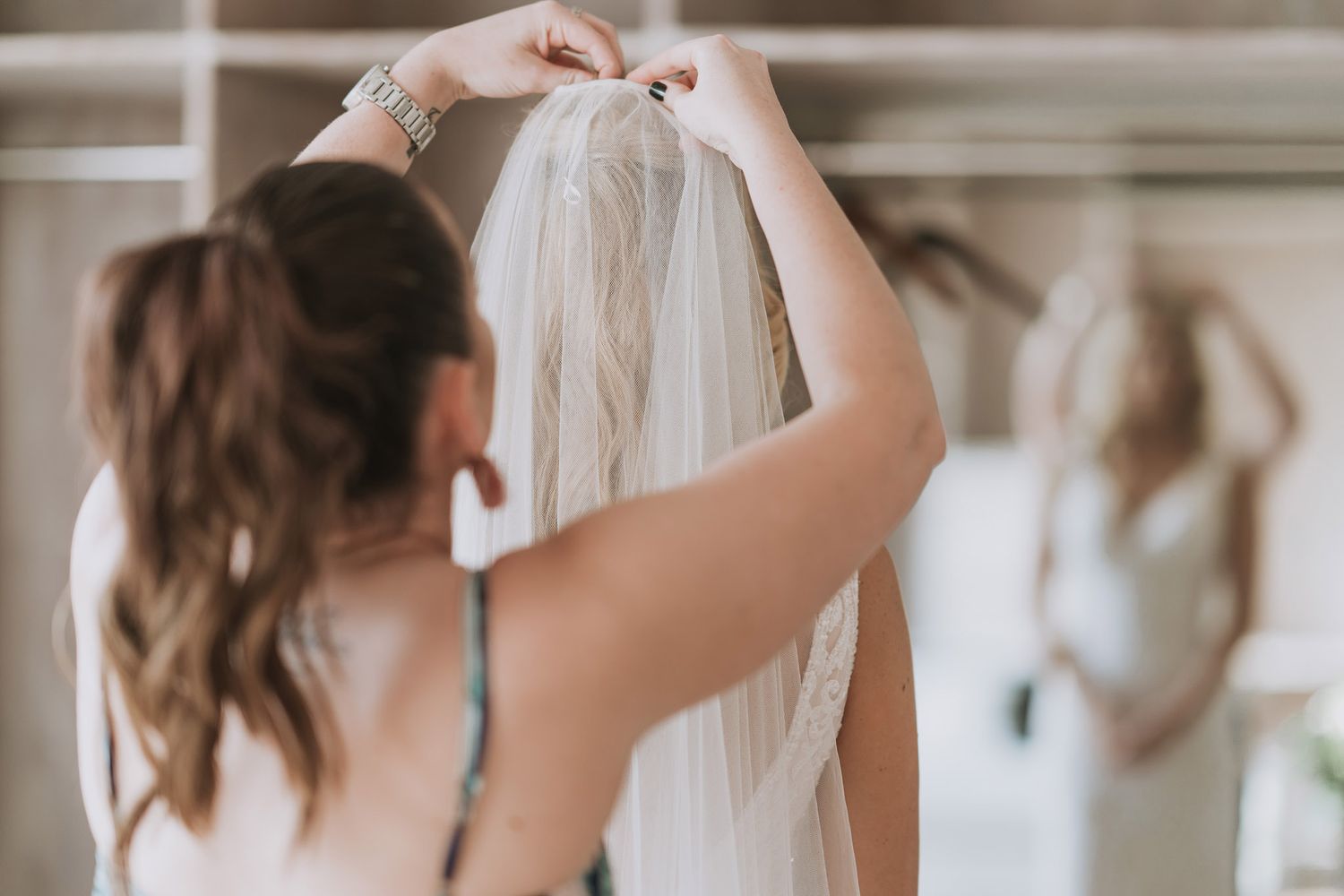 Row of bridesmaids' legs in nude shoes standing in front of an elegant wall during a wedding photoshoot.