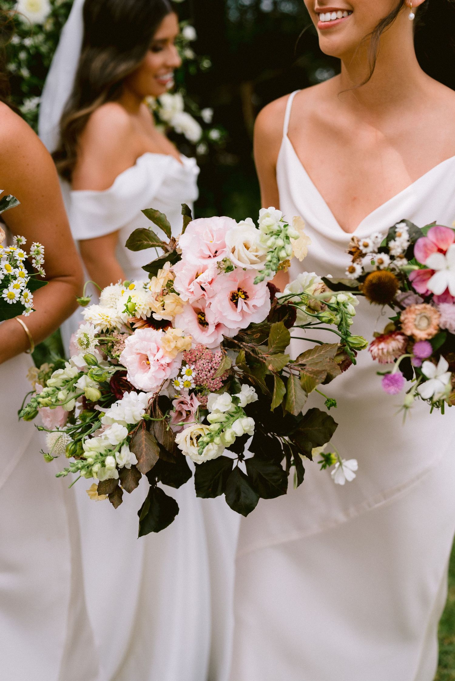 Bridesmaids in white dresses holding beautiful pink and green floral bouquets.