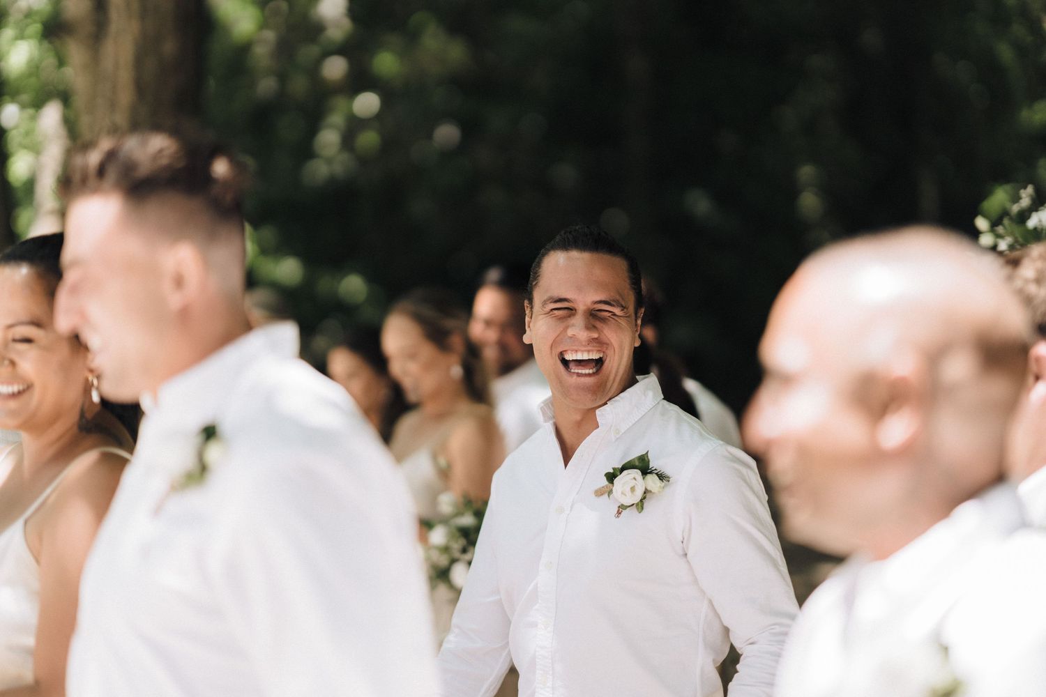 Wedding party members in white attire share joyful moments during an outdoor celebration.