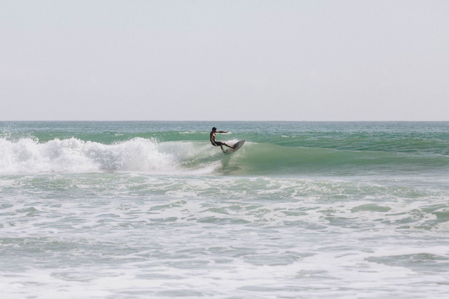 A surfer rides a wave on their surfboard in turquoise green ocean waters.