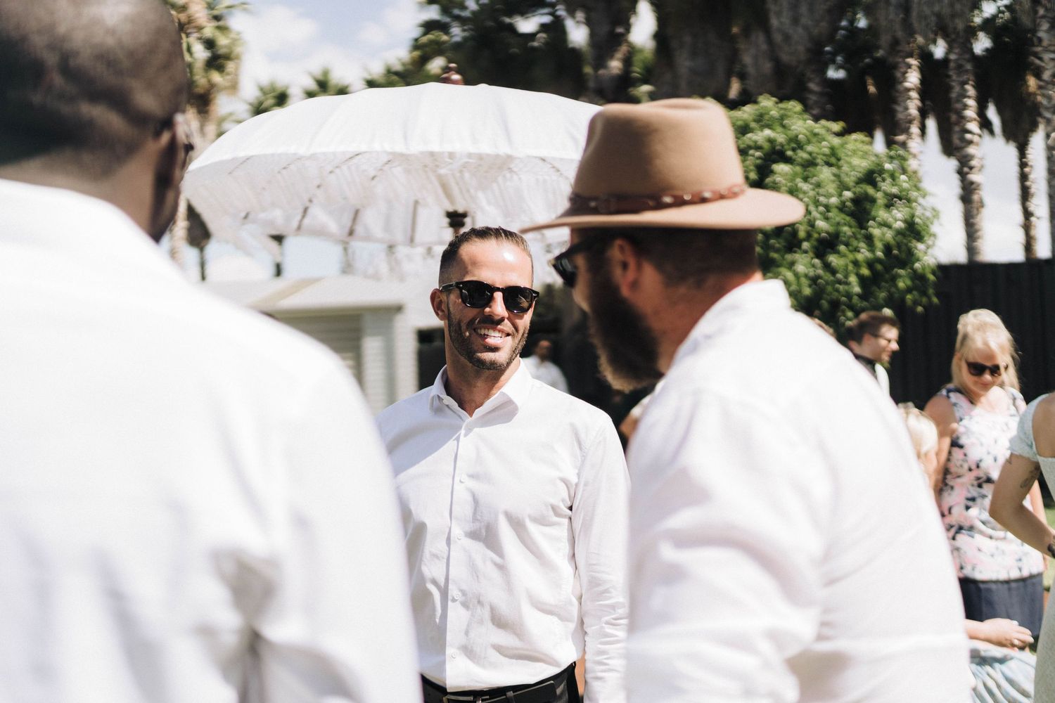 People in white attire and sunglasses socializing at outdoor summer event.