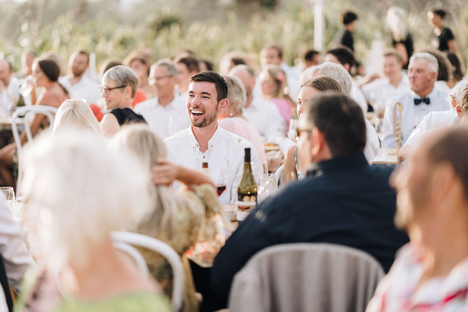 Wedding reception guests laugh and celebrate during an outdoor party under a tent.
