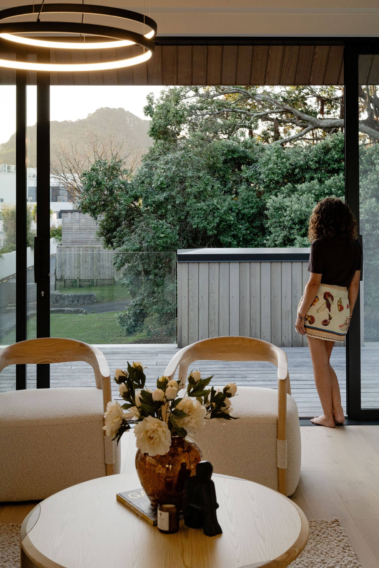 Modern dining room with circular pendant light, white table and chairs, floral centerpiece, and silhouetted figure by window.