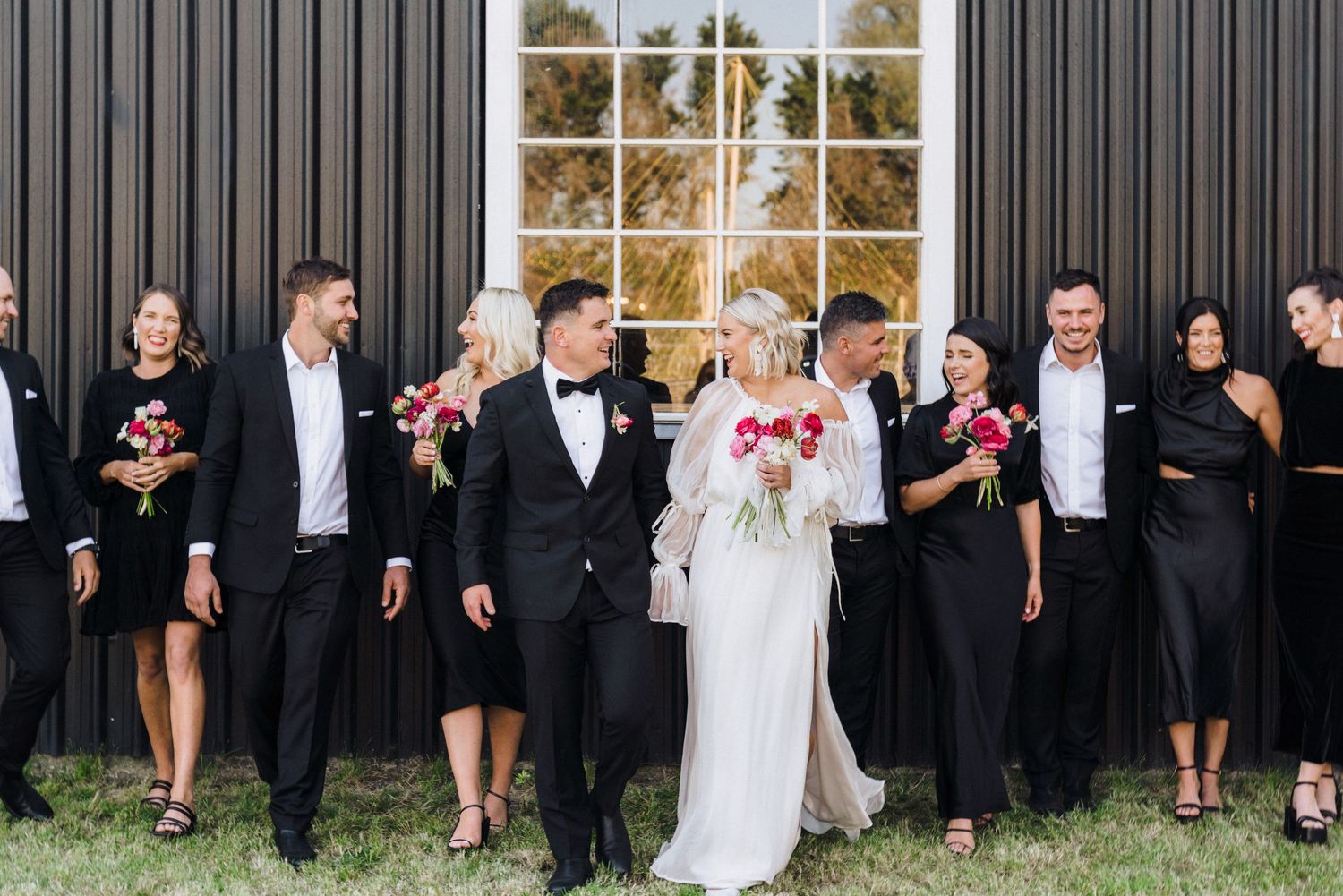 Wedding party in formal attire posing together outdoors against dark building.