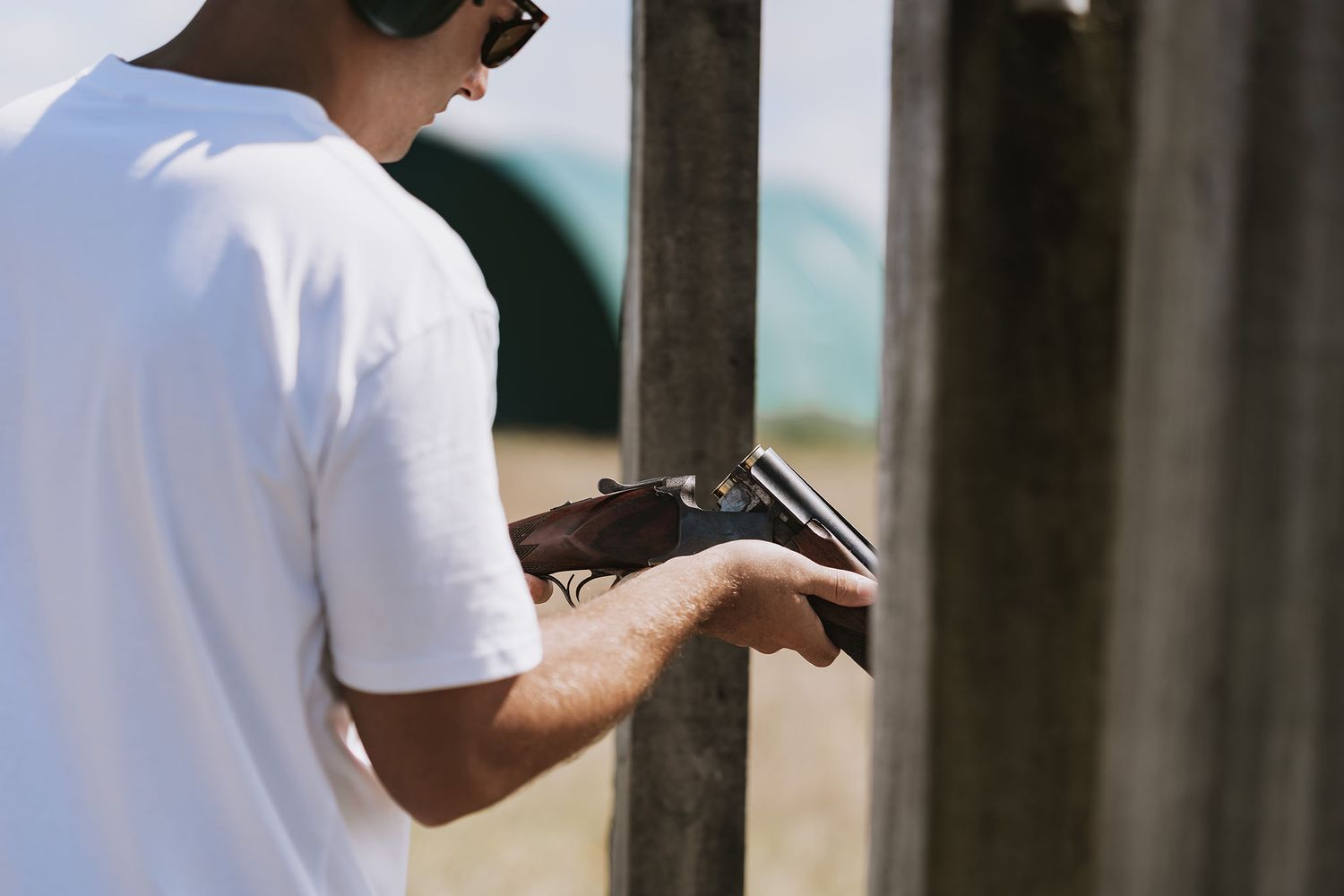 Person wearing a white t-shirt practicing at an outdoor shooting range with a pistol.