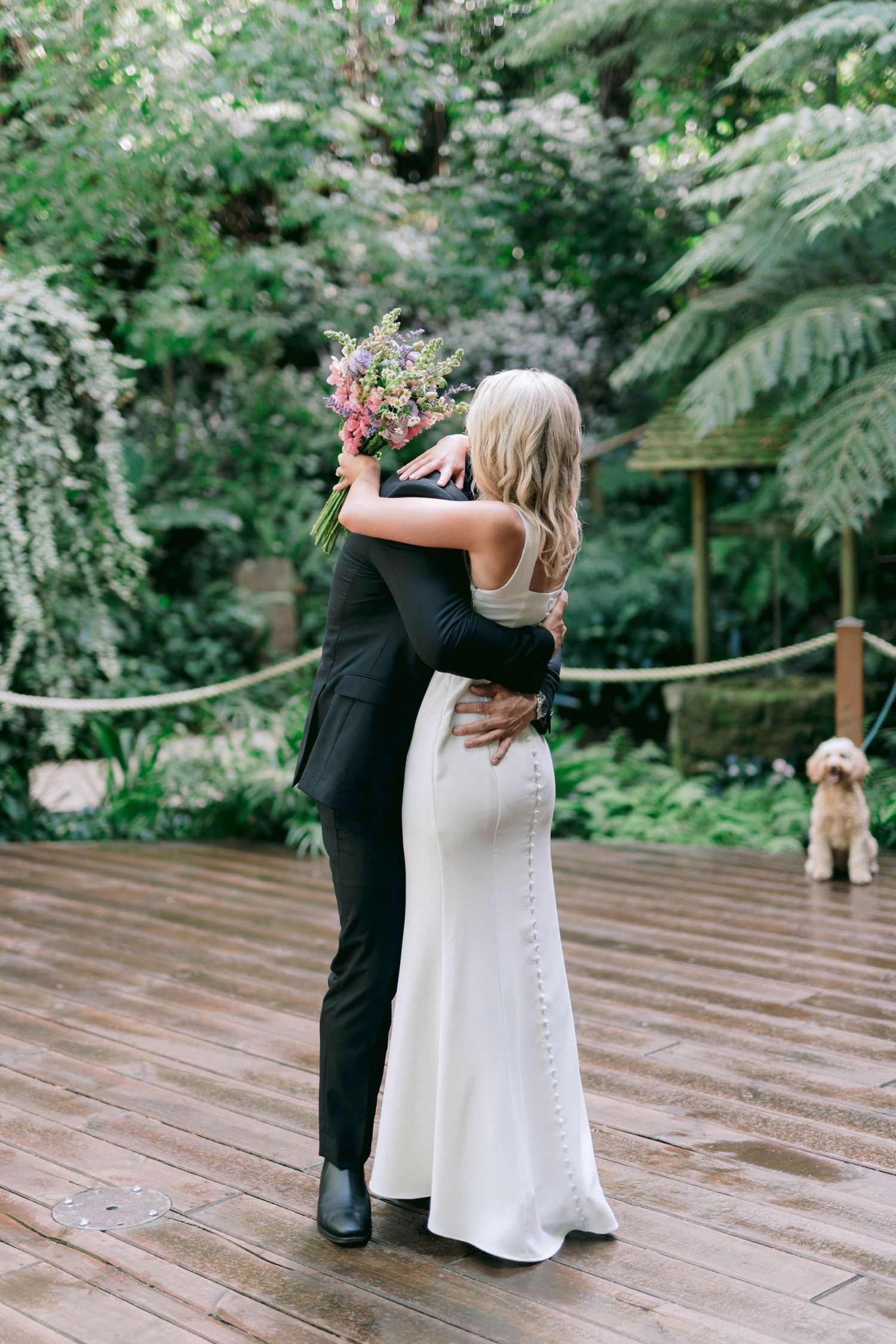 Reception guests taking synchronized shots of drinks on an outdoor wooden deck surrounded by lush greenery and twinkle lights.