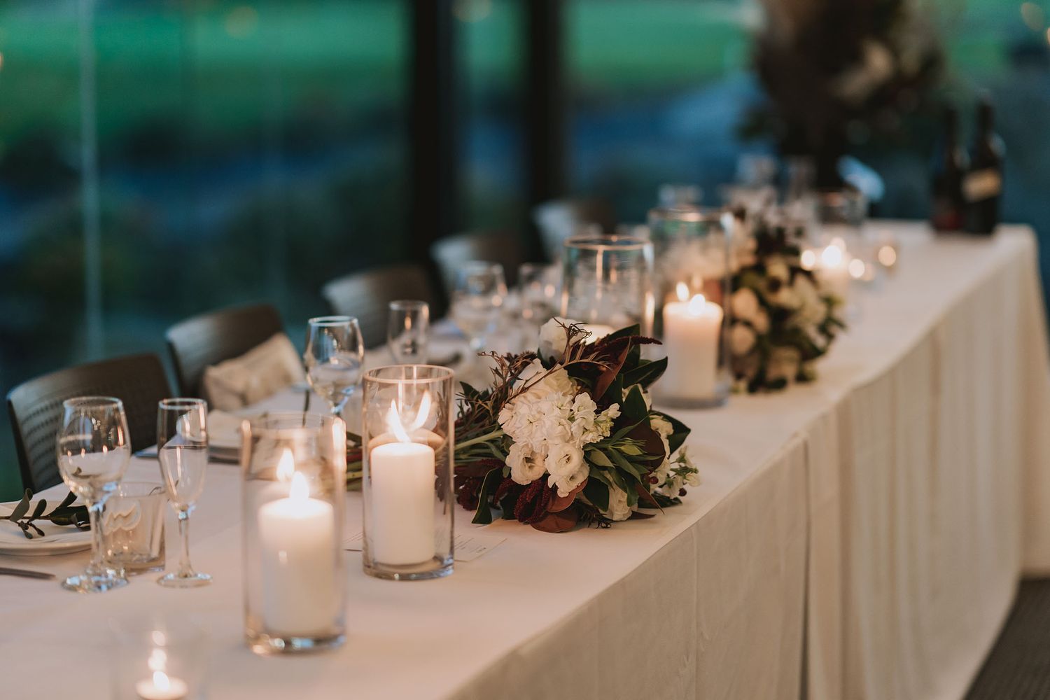 White wedding reception table decorated with glowing candles and floral arrangements against a turquoise backdrop.