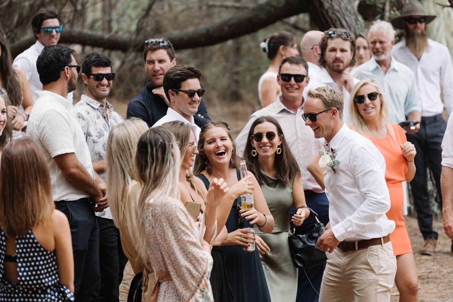 A group of stylishly dressed guests socializing at an outdoor event under trees.