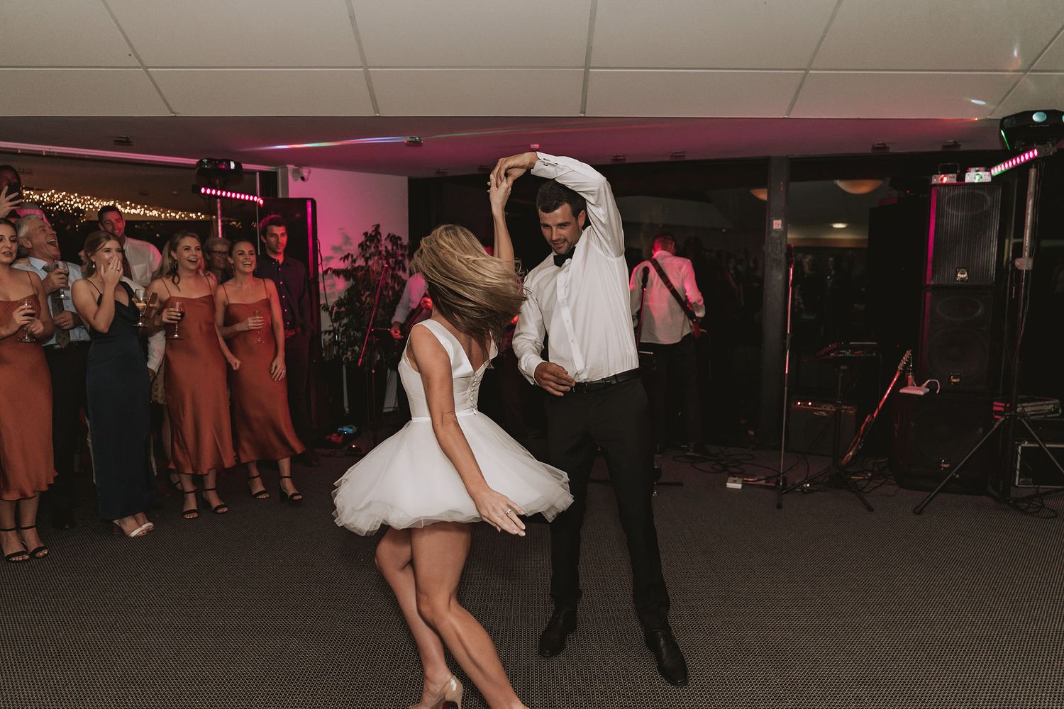 Two dancers perform an energetic swing dance routine on a dark dance floor with pink lighting in the background.