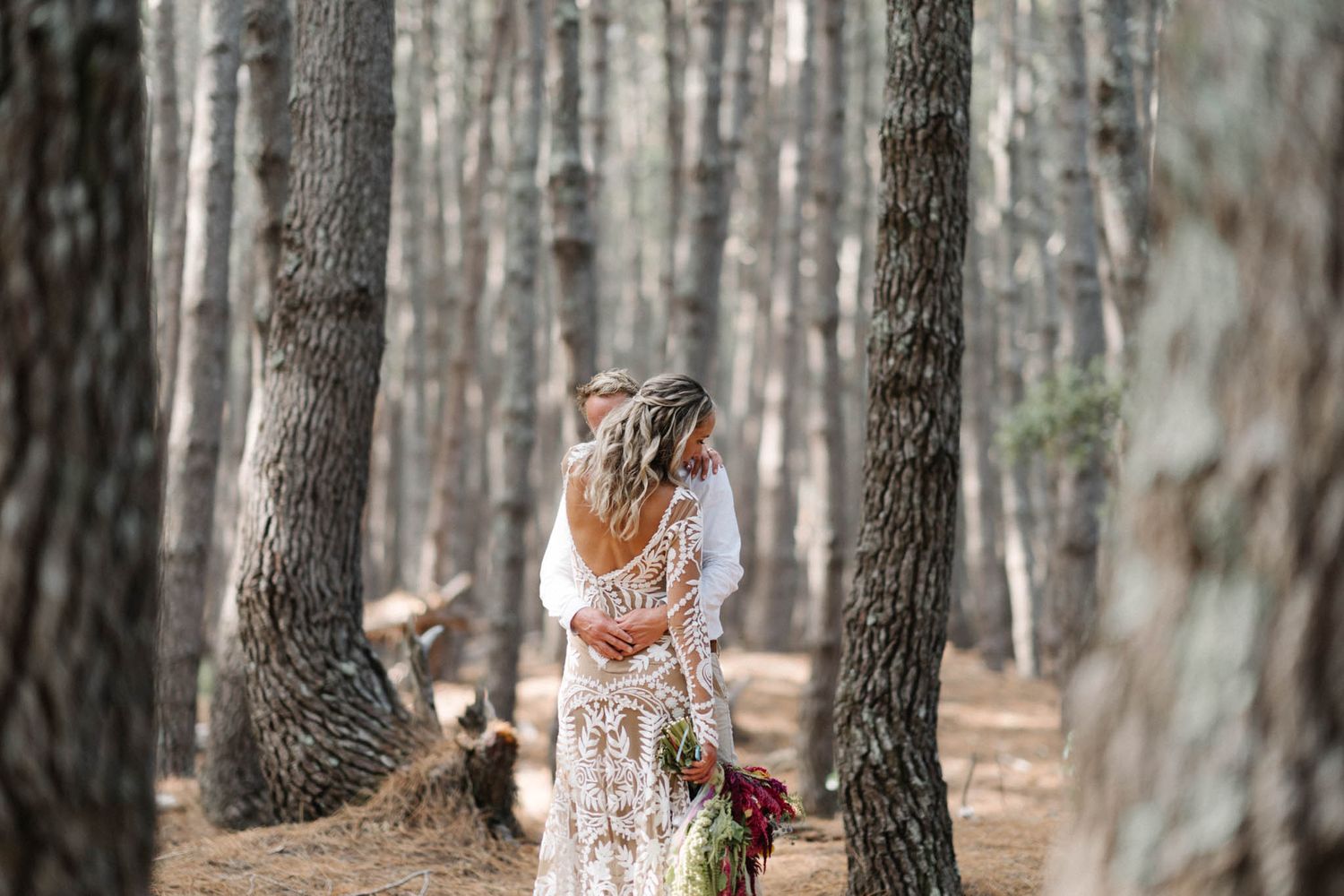 A white lace dress flows gracefully among tall pine trees in a serene forest setting.