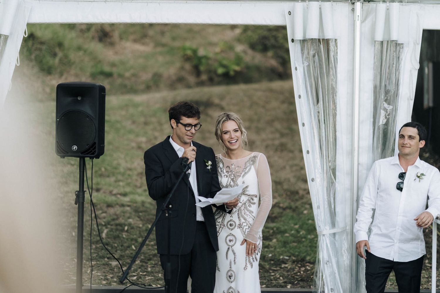 An outdoor wedding ceremony on a hill with a speaker setup and flowing white curtains framing the scene.