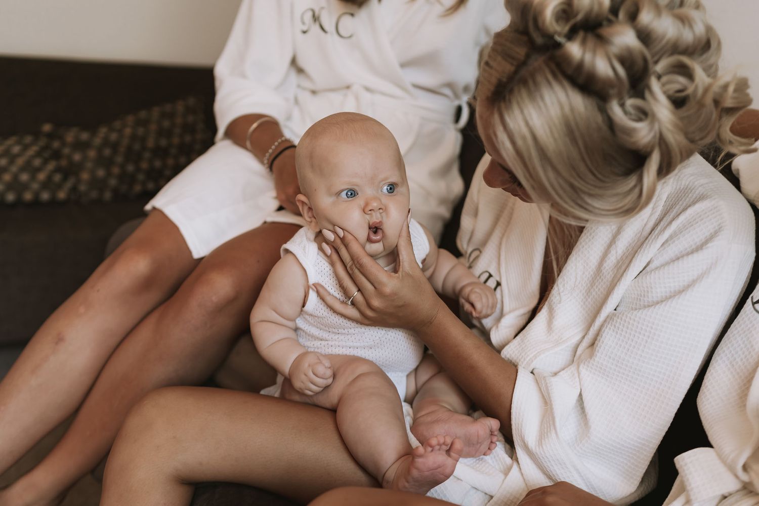 Gentle mother in white holds and kisses her newborn baby in tender moment against neutral background.