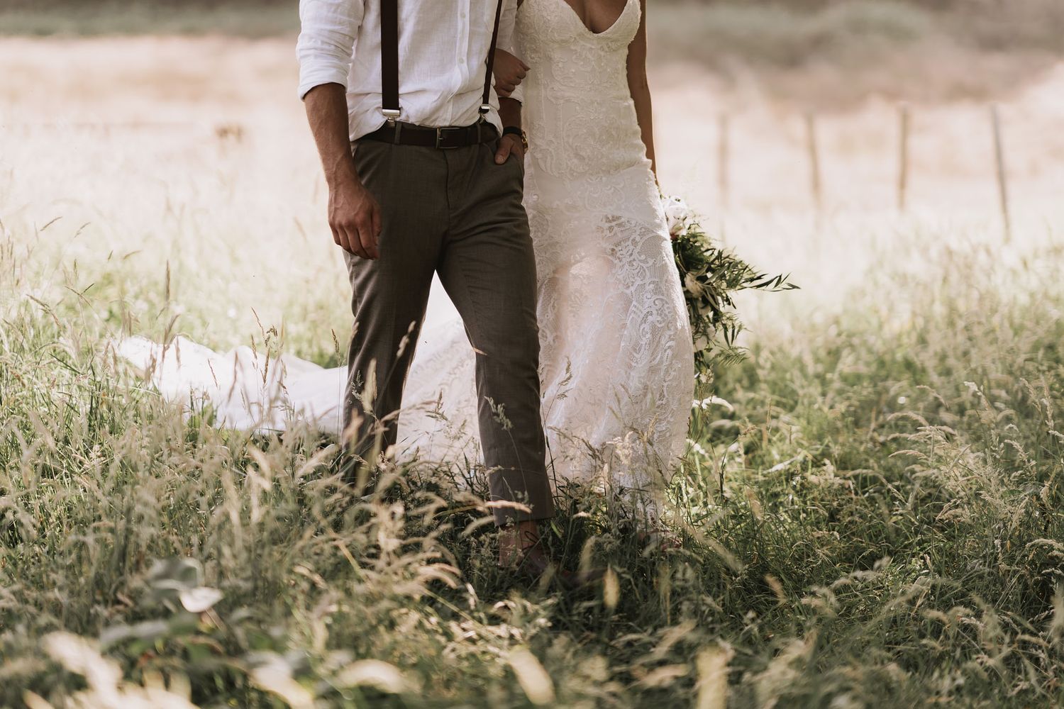 A bride and groom stand together in tall grass during a rustic outdoor wedding photoshoot.