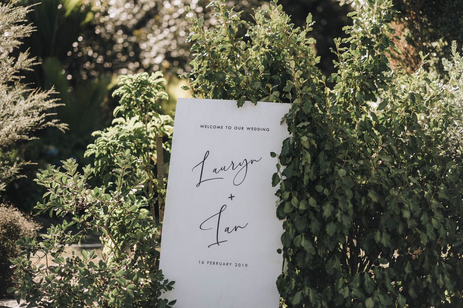 Wedding invitation cards with elegant calligraphy placed among lush green foliage and natural outdoor setting.