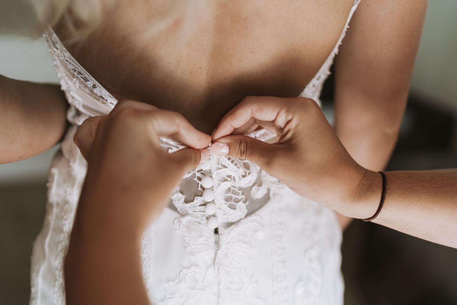 Close-up detail of hands fastening delicate white lace on a wedding dress.