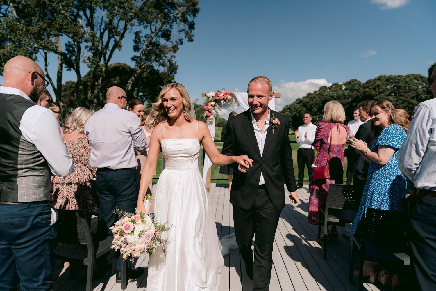 Outdoor wedding reception with guests mingling under blue sky and trees.