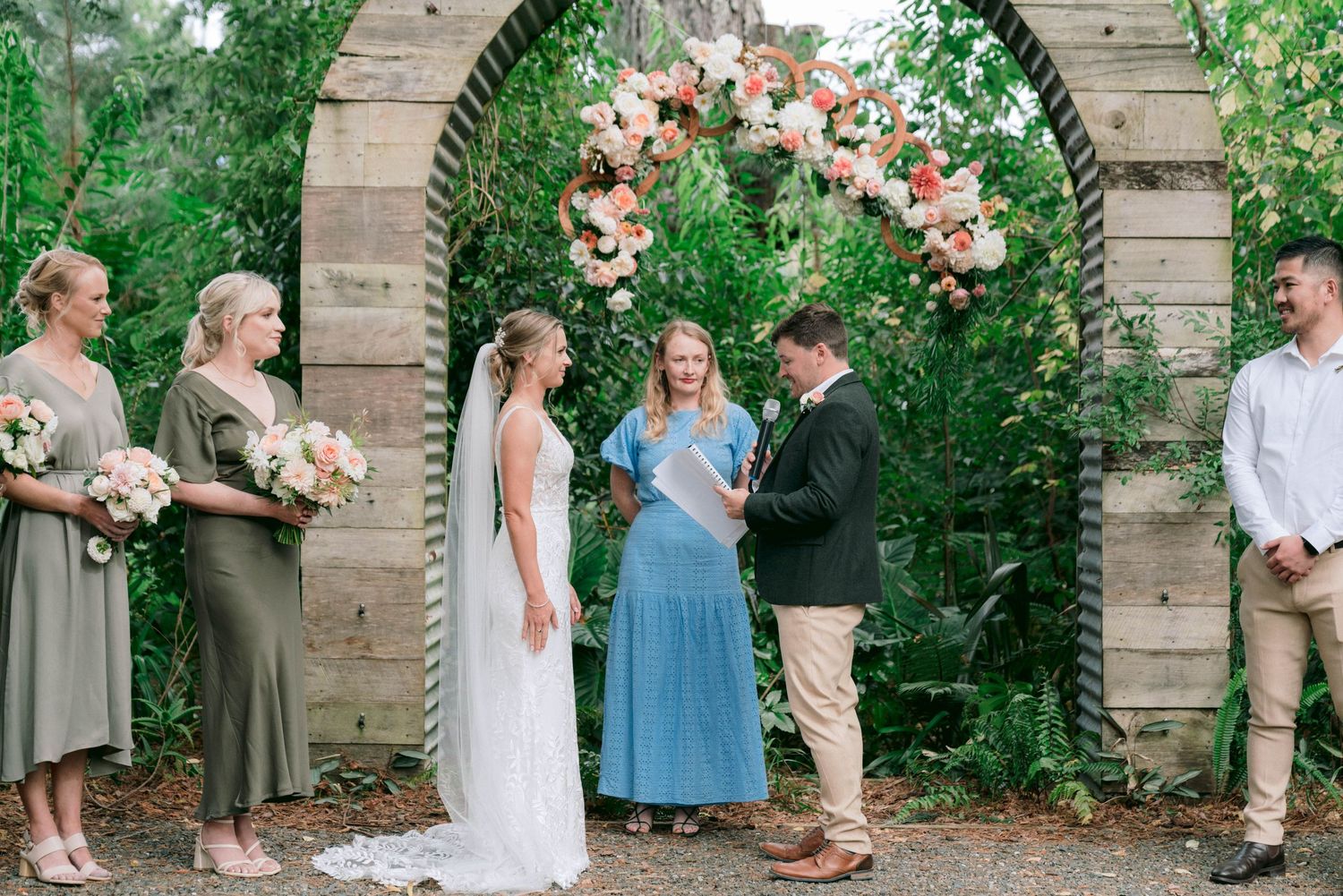 Wedding ceremony group photos taken under an ornate floral arch in a garden setting.