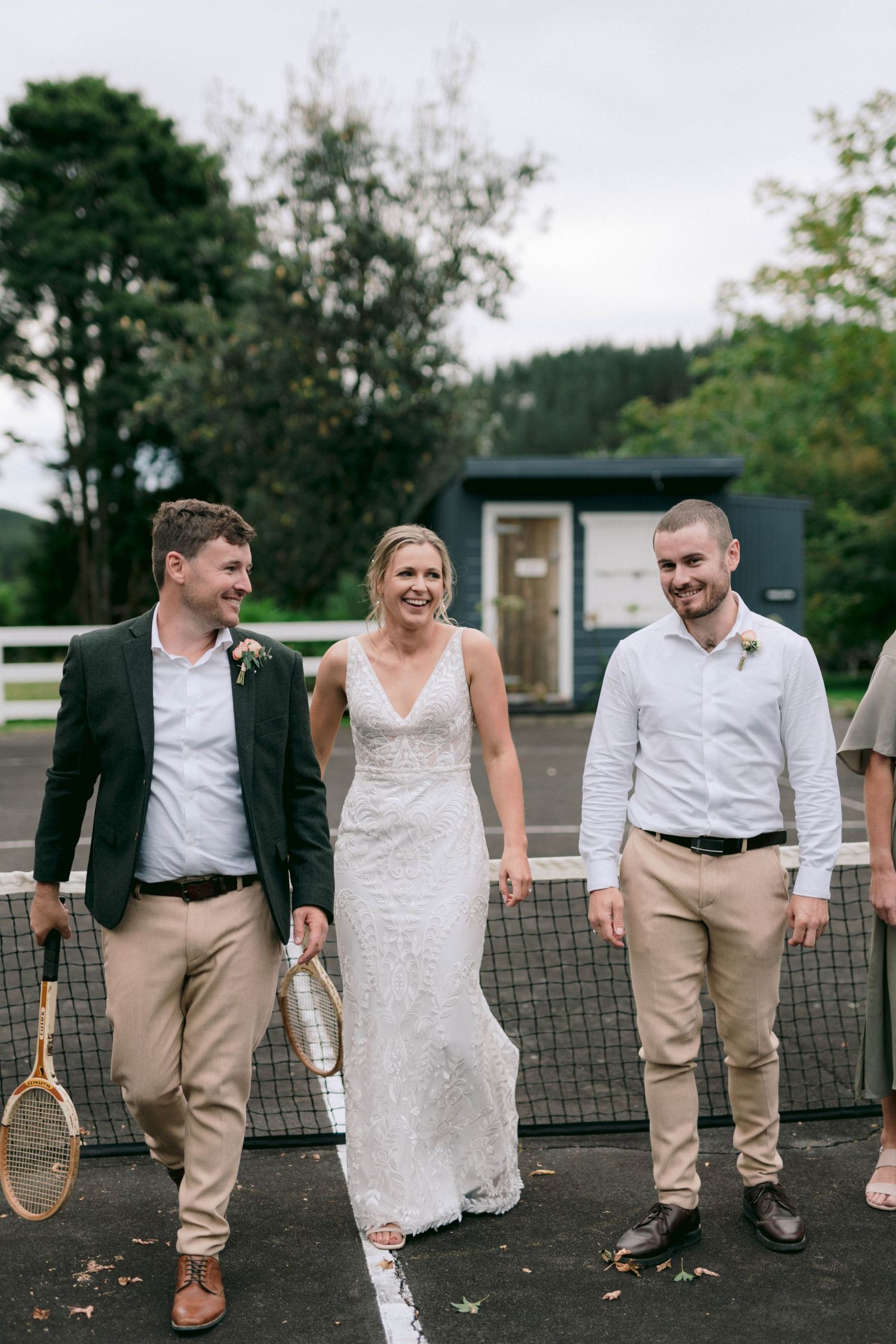 Wedding party walking together on a tennis court holding vintage rackets in casual attire.
