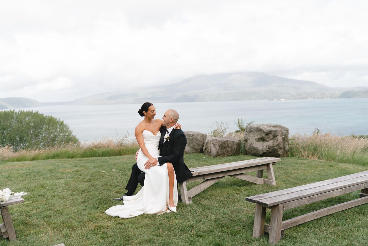 A couple shares an intimate moment on a wooden bench overlooking a misty coastal landscape.